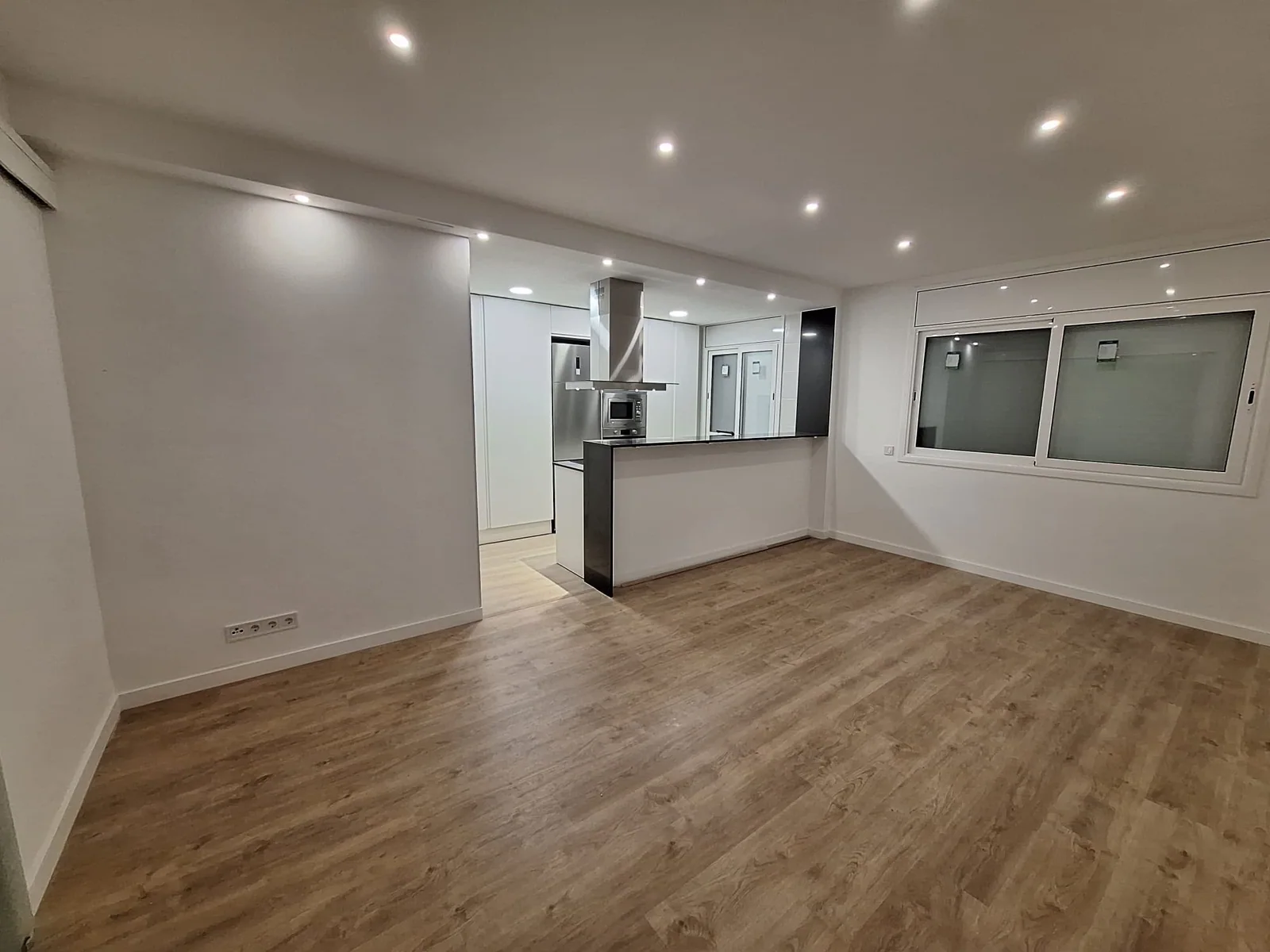 Espacio reformado con cocina abierta, suelo de madera e iluminación empotrada